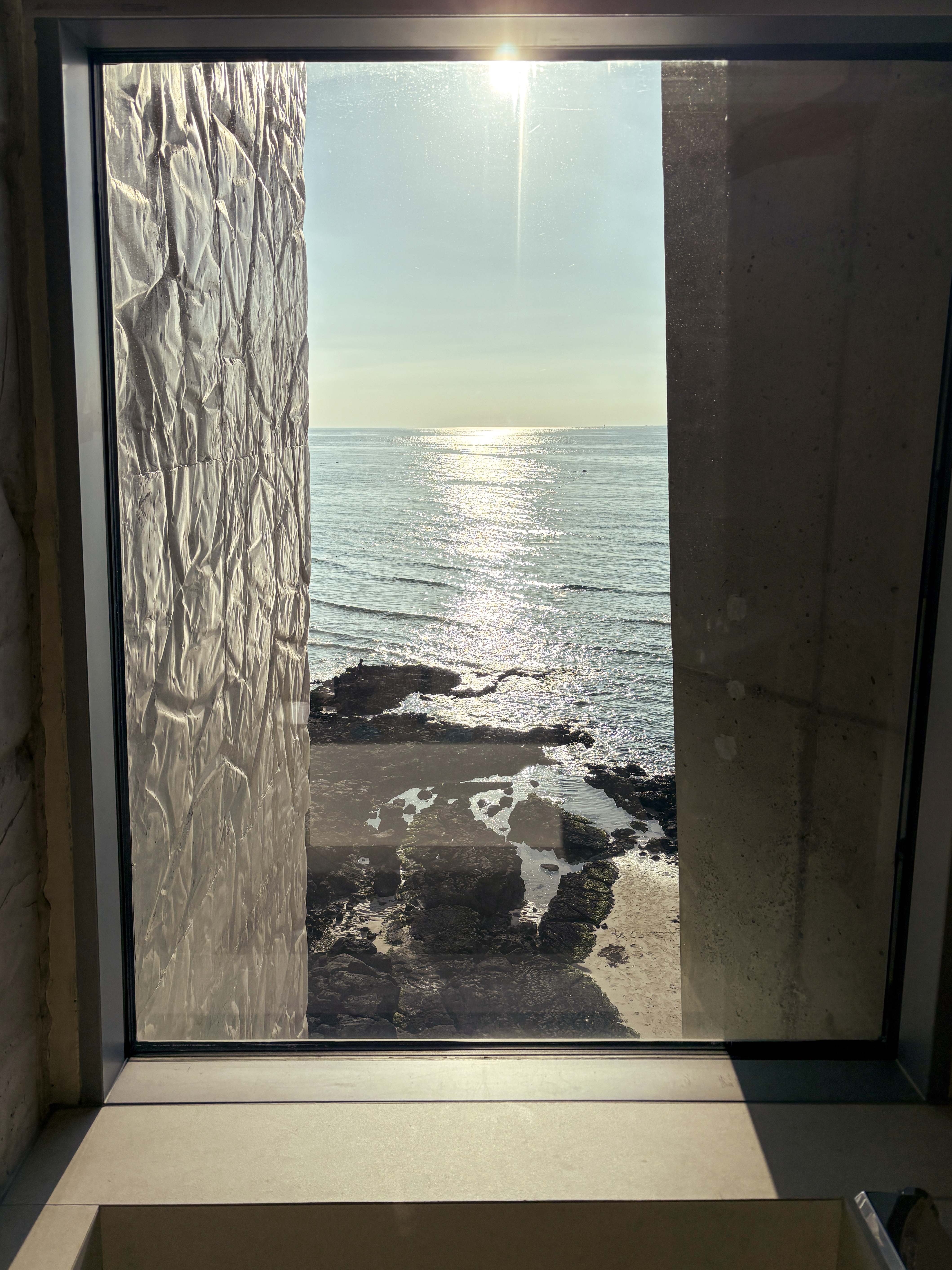 A bath, a window, an ocean, and a sun, all in a straight line from the camera lens.